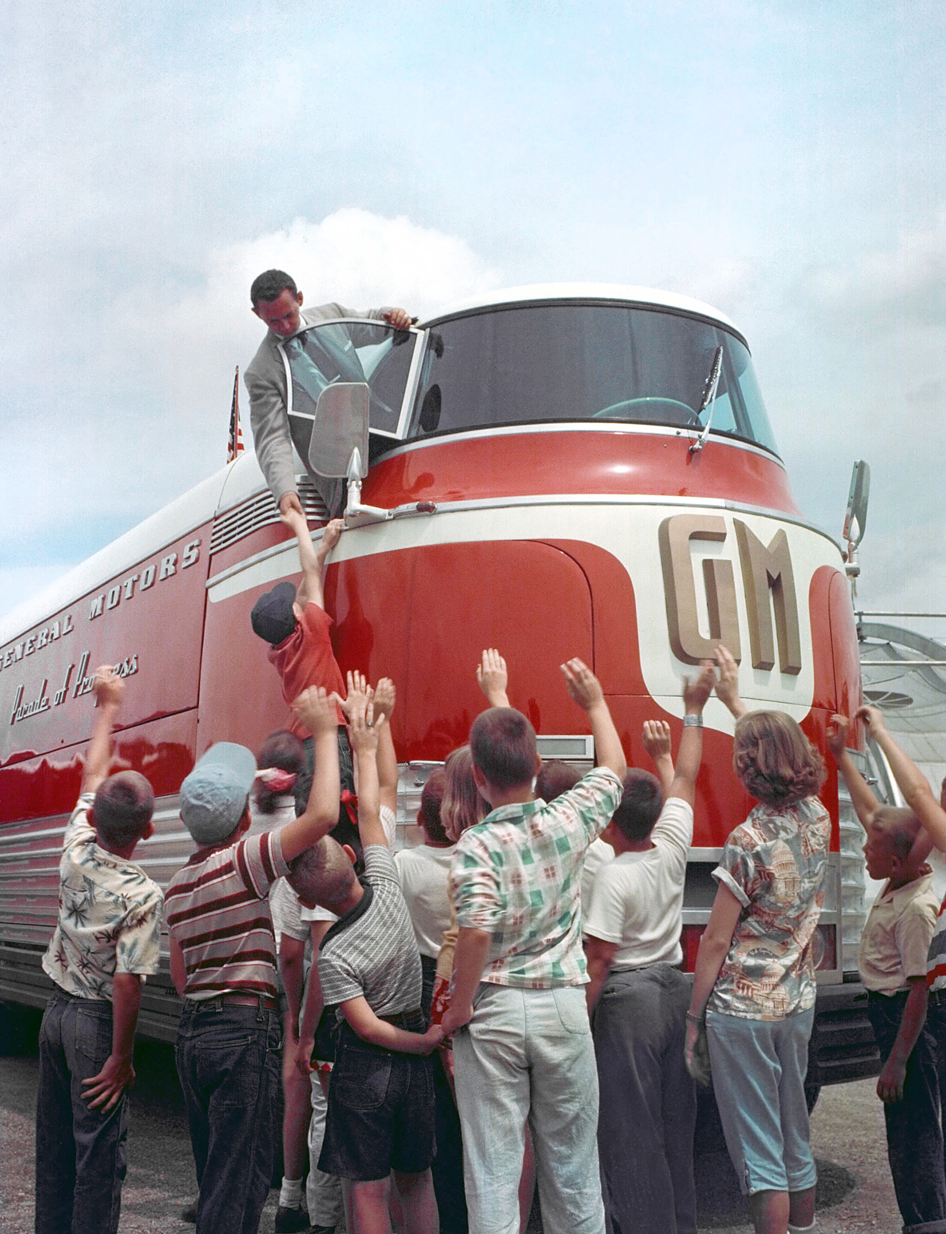 a driver leans out of a Futurliner's window to shake the hand of a child who's been boosted up