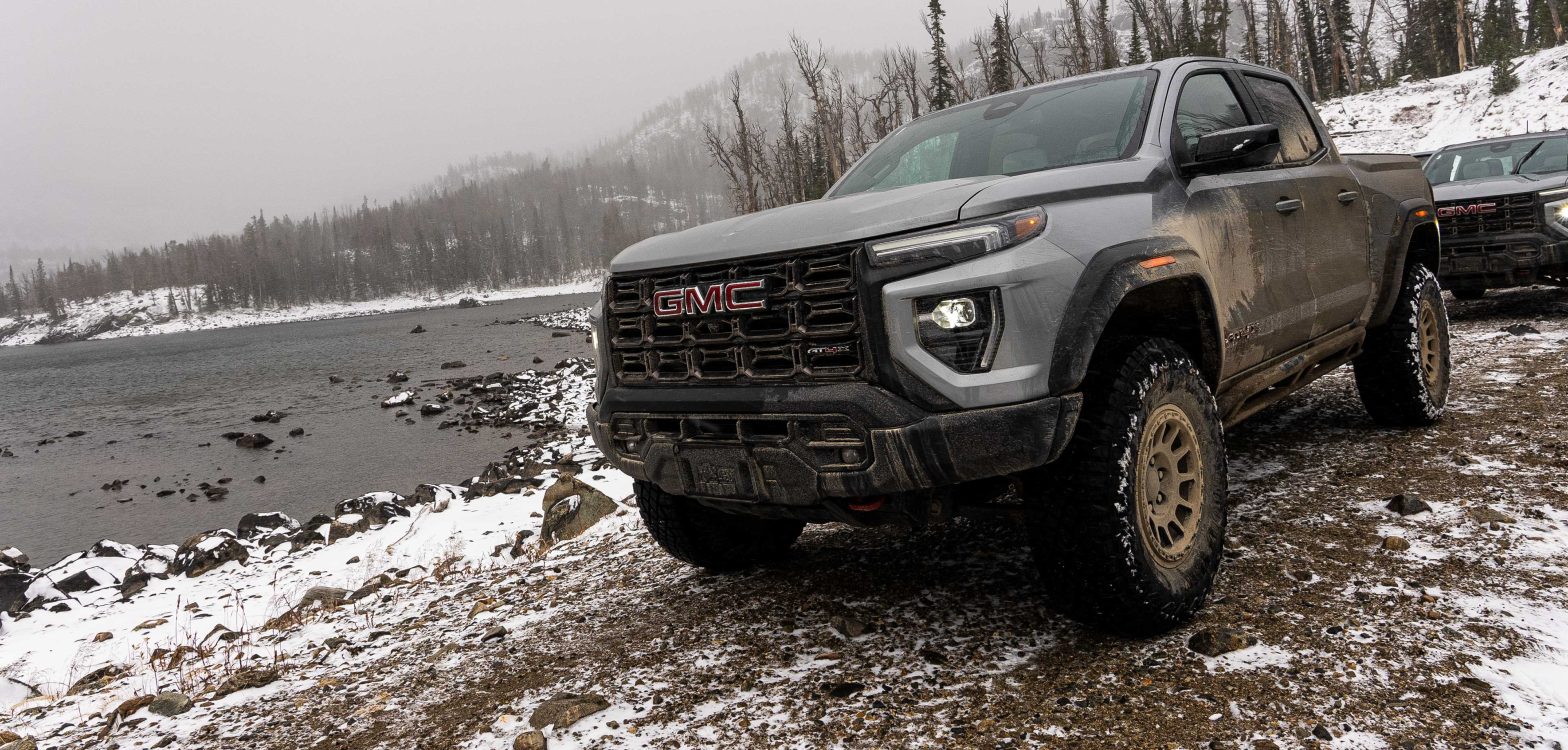 A GMC Canyon AT4X Off Road Next To A Frozen Lake In A Snowy Mountain Landscape