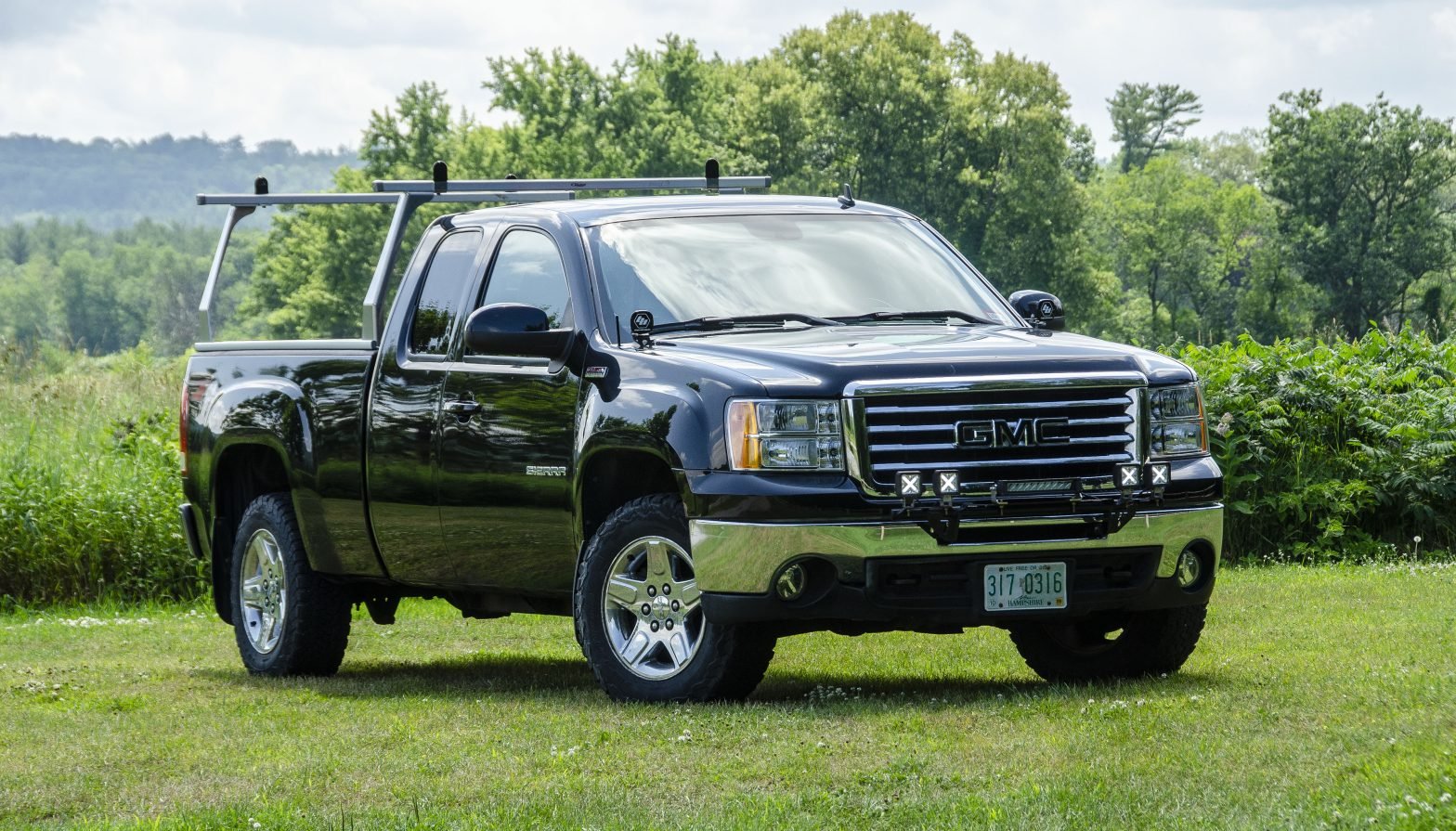 A 2011 GMC Sierra in front of a field- equipped with a bed rack and off-road lighting