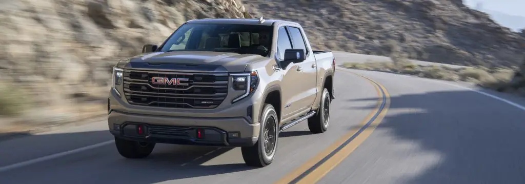 The 2023 GMC Sierra AT4X driving on pavement finished in Desert Sand Metallic.