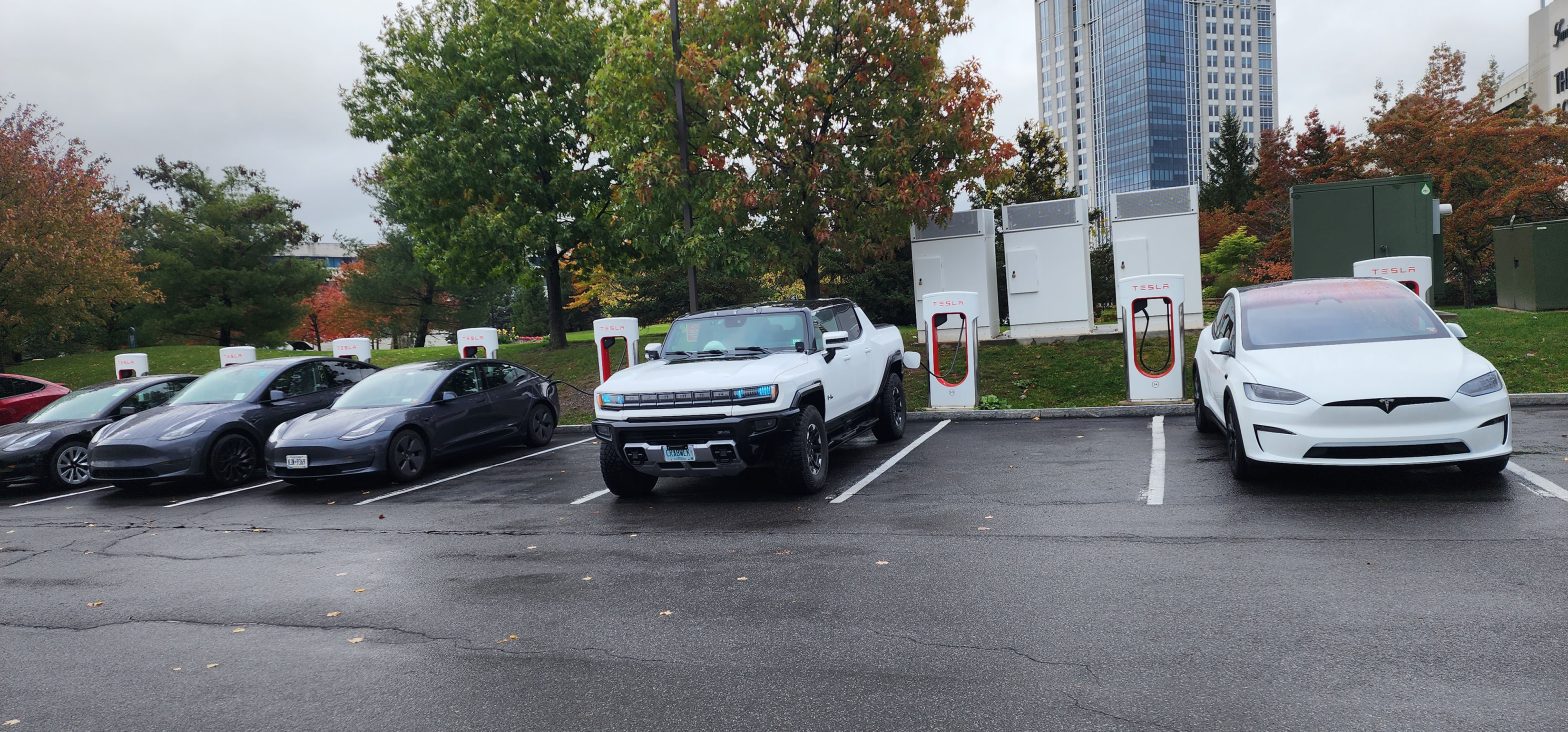 The GM-TRucks.com GMC HUMMER EV SUT charging at a Tesla Supercharger Station surrounded by Tesla cars