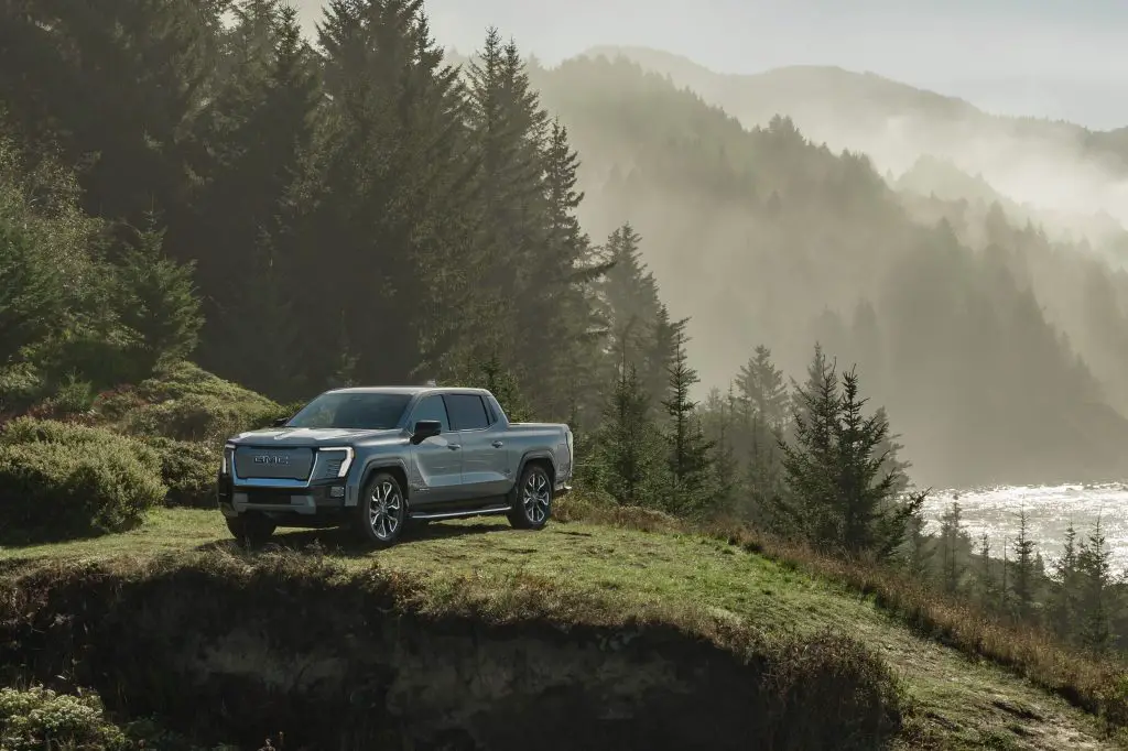 Front 3/4 view of the 2024 GMC Sierra EV Denali Edition 1 in Thunderstorm Grey on a wooded cliff.
