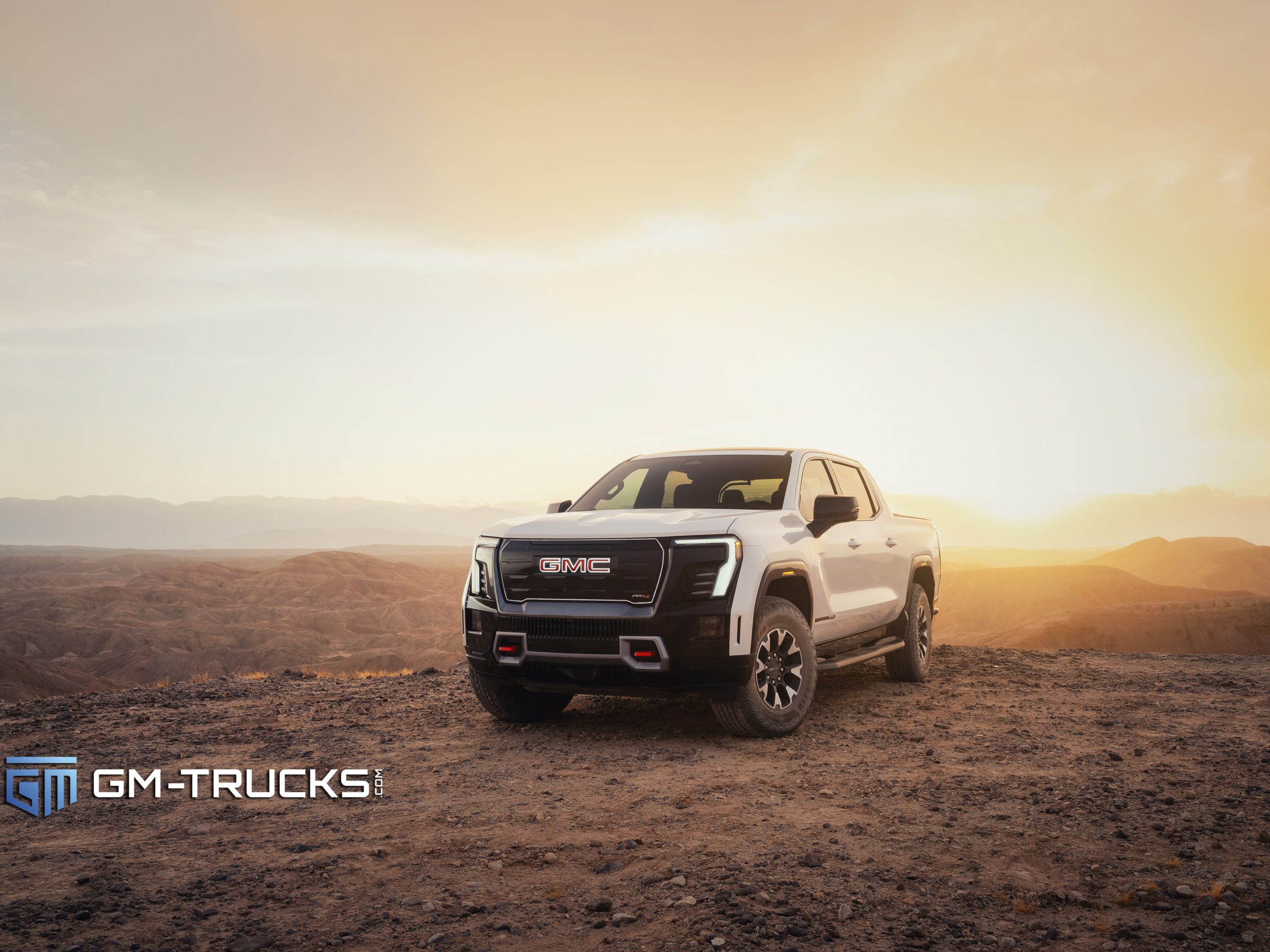 Still Don’t Trust EV Trucks? The 2026 GMC Sierra EV Is Built to Change That With A Lower Price & More Trims 5 A white 2026 GMC Sierra EV AT4 parked on rocky terrain at sunset, highlighting its lifted stance, 35-inch tires, and off-road design.