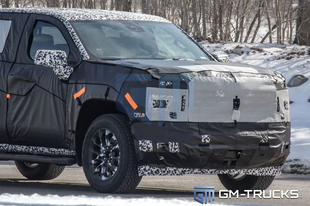 Close-up of a camouflaged 2027 Chevrolet Silverado or GMC Sierra prototype front end, showing hidden grille, headlights, and bumper design.