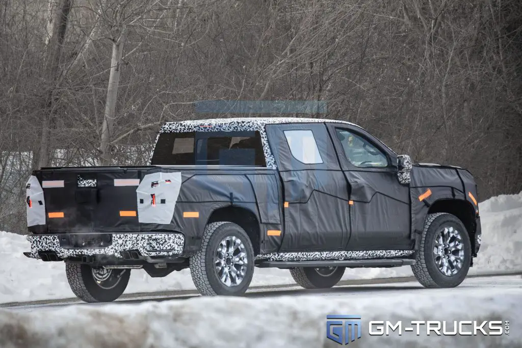 Camouflaged 2027 Chevrolet Silverado or GMC Sierra prototype spotted testing in winter conditions, showcasing updated rear-end design, taillights, and quad-tip exhaust.