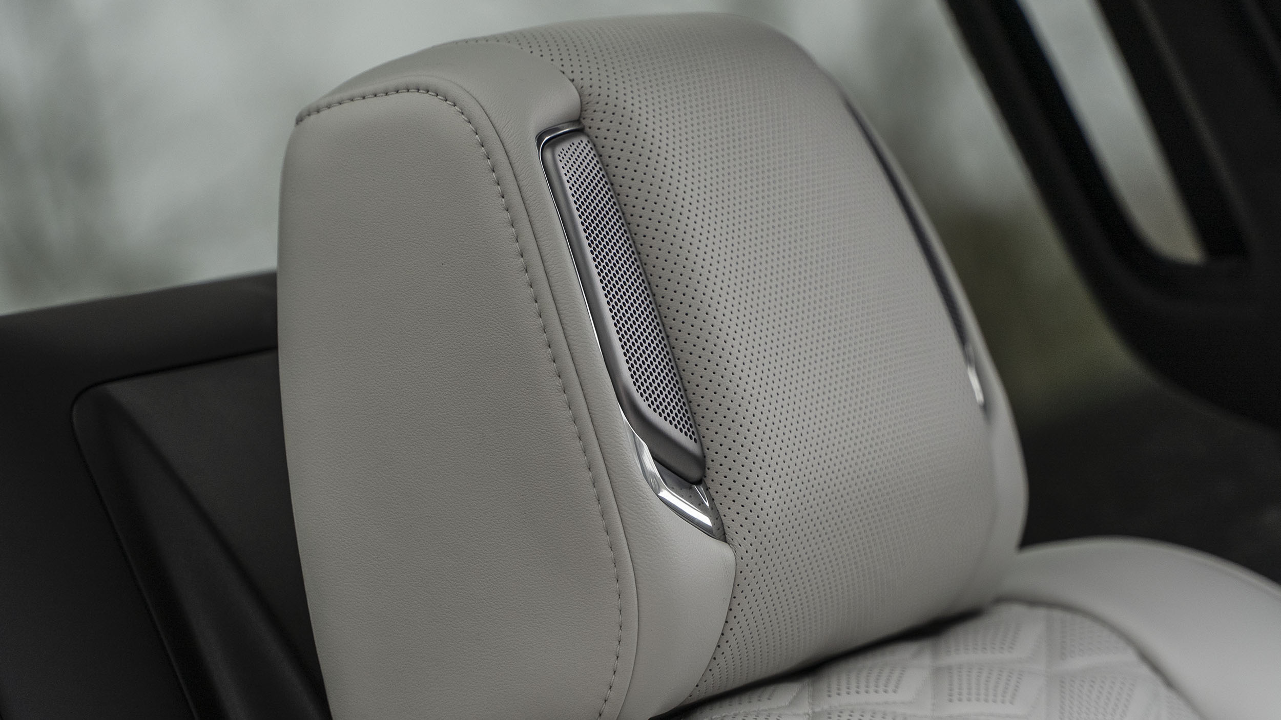 Power Open Doors, Night Vision & 55-Inch Displays: 5 Wild Tech Features on the 2026 Escalade 4 A close-up detail shot of the light grey perforated leather headrest in the 2026 Cadillac Escalade, showing the integrated metallic AKG speaker grille on the side.