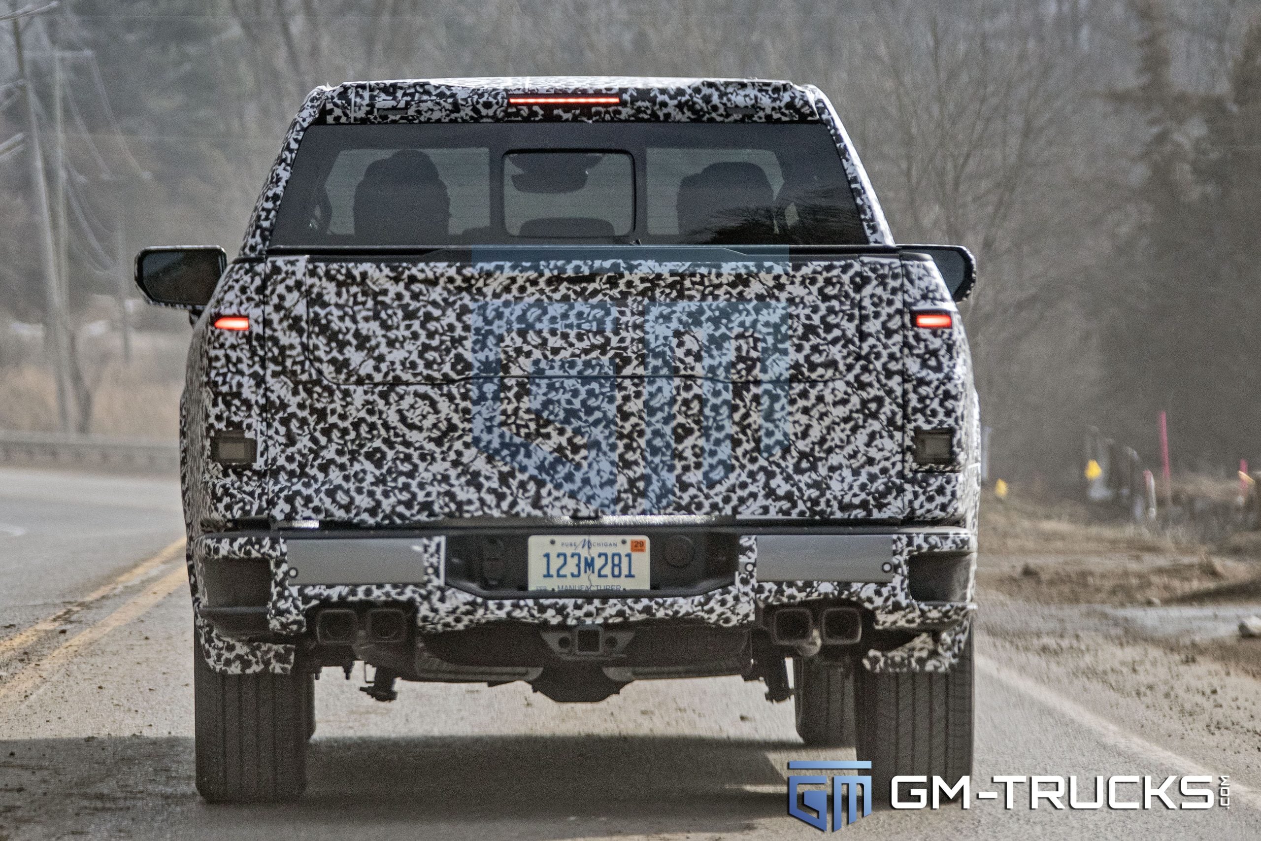 SPY SHOTS: 2027 GMC Sierra 1500 Denali & AT4 Break Cover – Full Interior Exposed! 5 Rear view of a camouflaged 2027 GMC Sierra 1500 prototype showing an integrated quad-exhaust system and new MultiPro tailgate cut-lines.