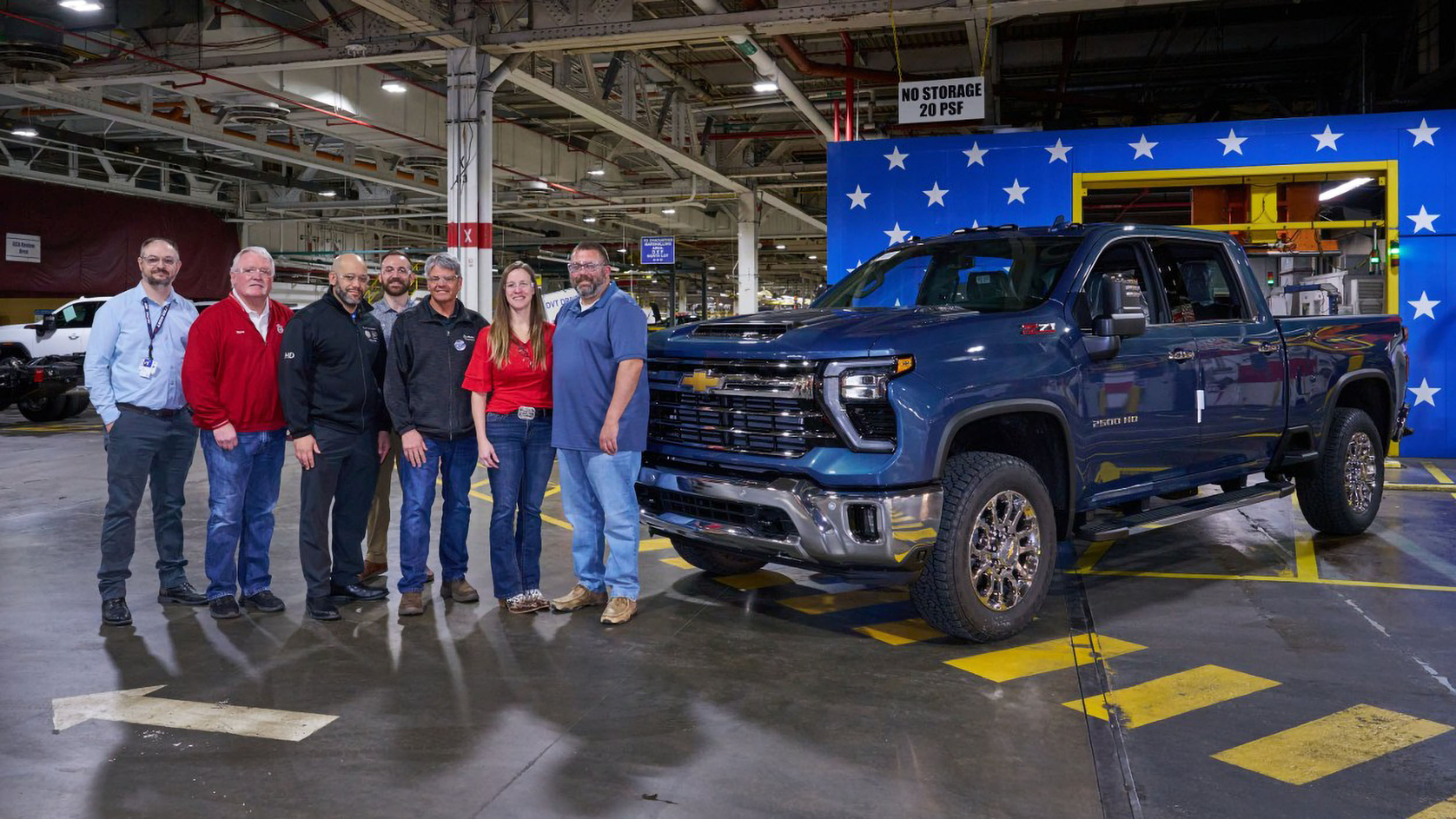 American Made: 27 Million Trucks Built at Fort Wayne and Flint 3 A group of seven people, including the new owners and plant leadership, stand next to the 16 millionth vehicle from Flint Assembly. The truck is a Lakeshore Blue Metallic Chevrolet Silverado 2500 HD LTZ with Z71 badging, parked inside the factory near a patriotic star backdrop.
