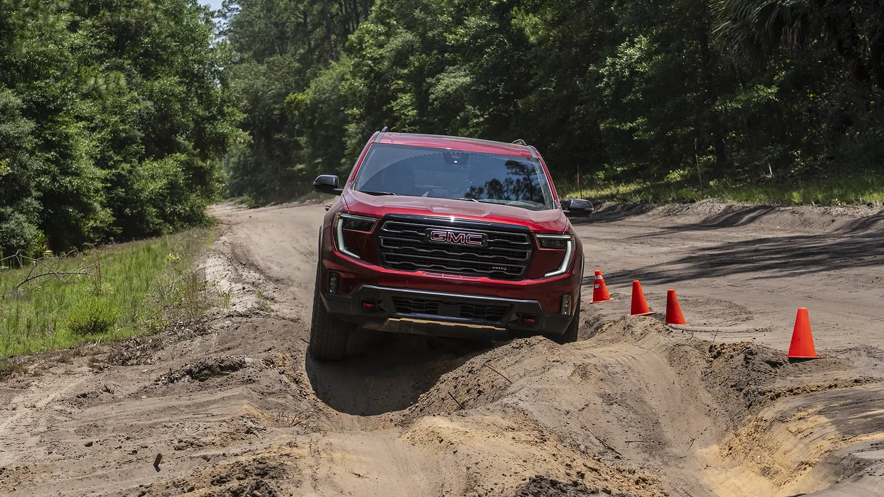 2027 GMC Acadia Updates: Standard Denali Super Cruise, Interior Camera & AT4 Reserve 3 A red GMC Acadia AT4 driving on a wooded dirt road, showcasing the rugged trim that receives the new AT4 Reserve Package for the 2027 model year.