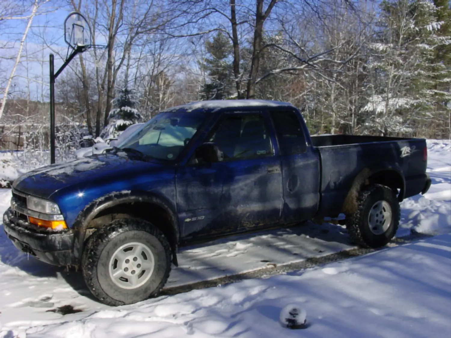 1996 Chevy Blazer vs 2026 Blazer: Epic Head-to-Head Crash 2 A dark blue 1999 Chevrolet S-10 ZR2 extended cab pickup truck parked in a snowy driveway next to a basketball hoop on a sunny winter day.