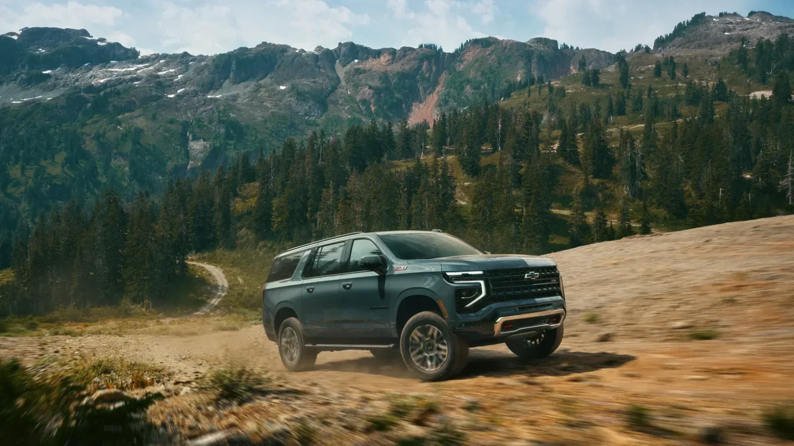 2027 Chevrolet Suburban Z71 in blue-gray driving on a dirt mountain trail