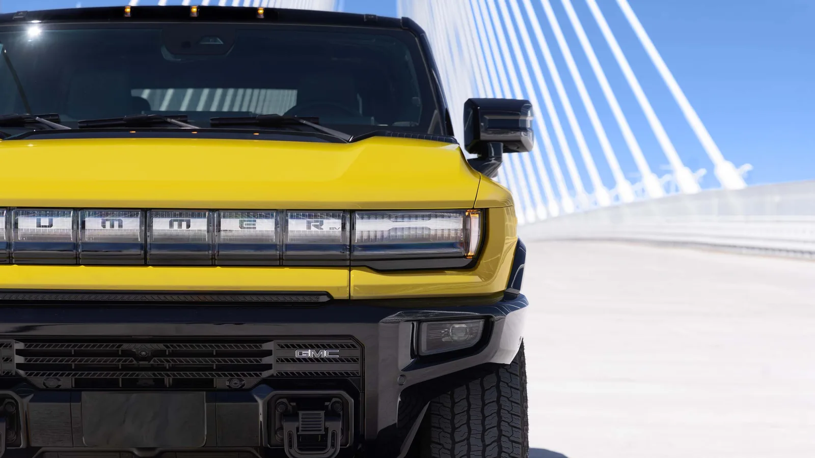Hummer Turns 25 and GMC Brought the H2's Yellow Back 2 Front view of a yellow 2027 GMC HUMMER EV ICON 25 with black front approach shield and illuminated HUMMER grille lighting