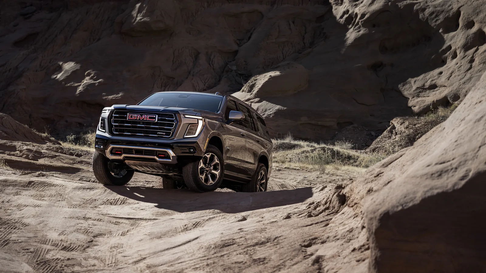 What's New for the 2027 GMC Yukon and Yukon XL 2 2027 GMC Yukon AT4 climbing over slickrock in a desert canyon