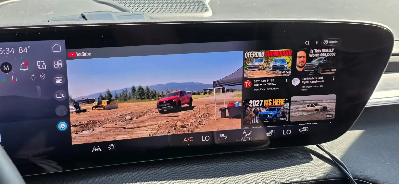 A wide panoramic dashboard view of the native YouTube app streaming a truck review video on a Buick Enclave's ultra-wide infotainment display screen.