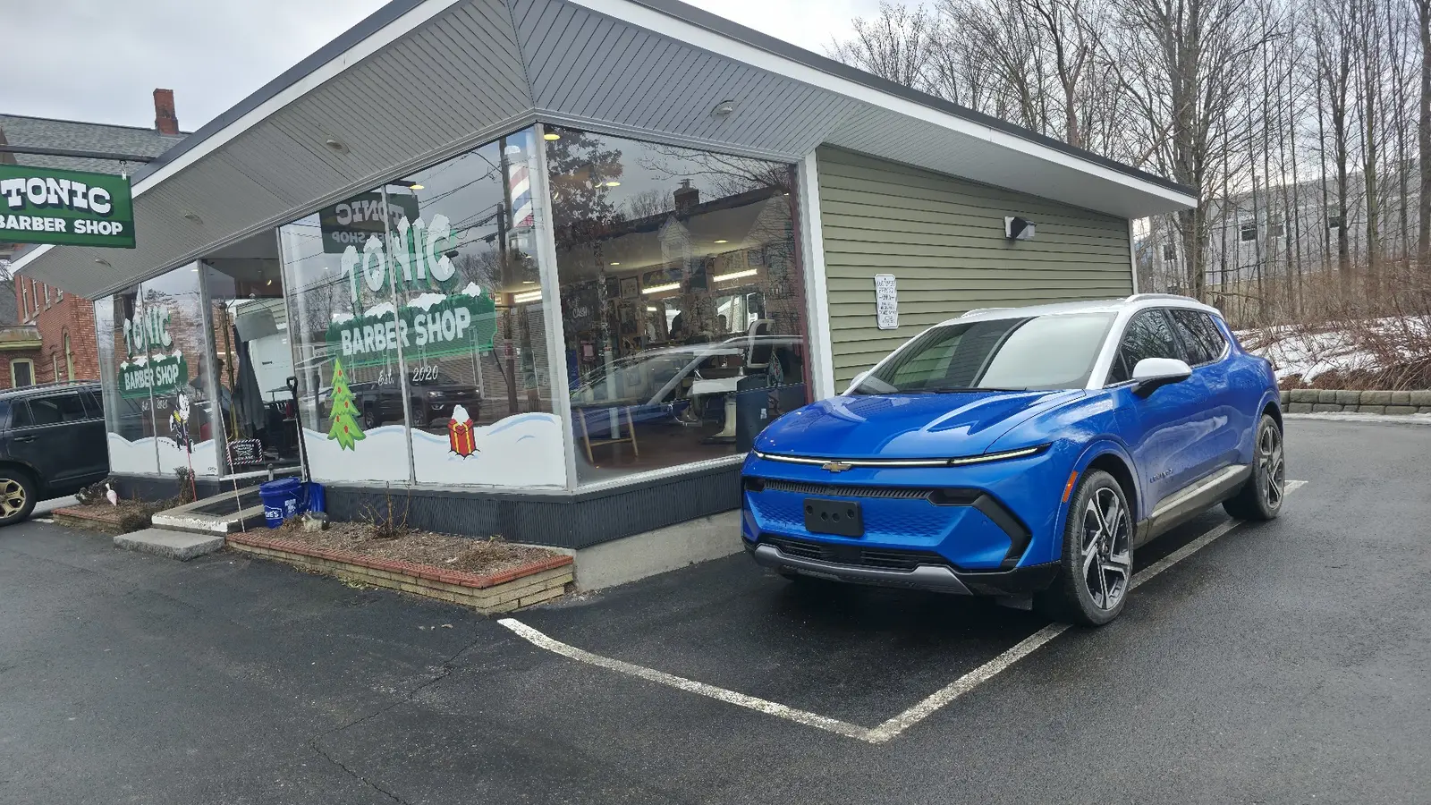 GM Ends Mandatory Vehicle-Wide Programming on EVs 3 Bright blue Chevrolet Equinox EV parked outside a barber shop storefront in winter