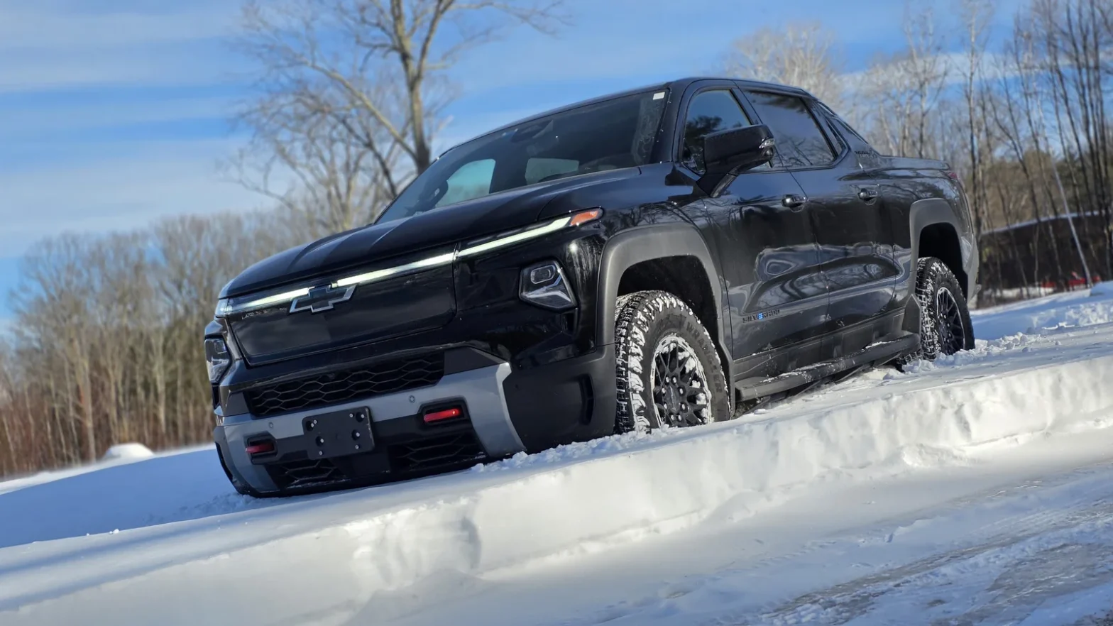 Black Chevrolet Silverado EV Trail Boss parked on a snowy road with bare trees and blue sky in the background
