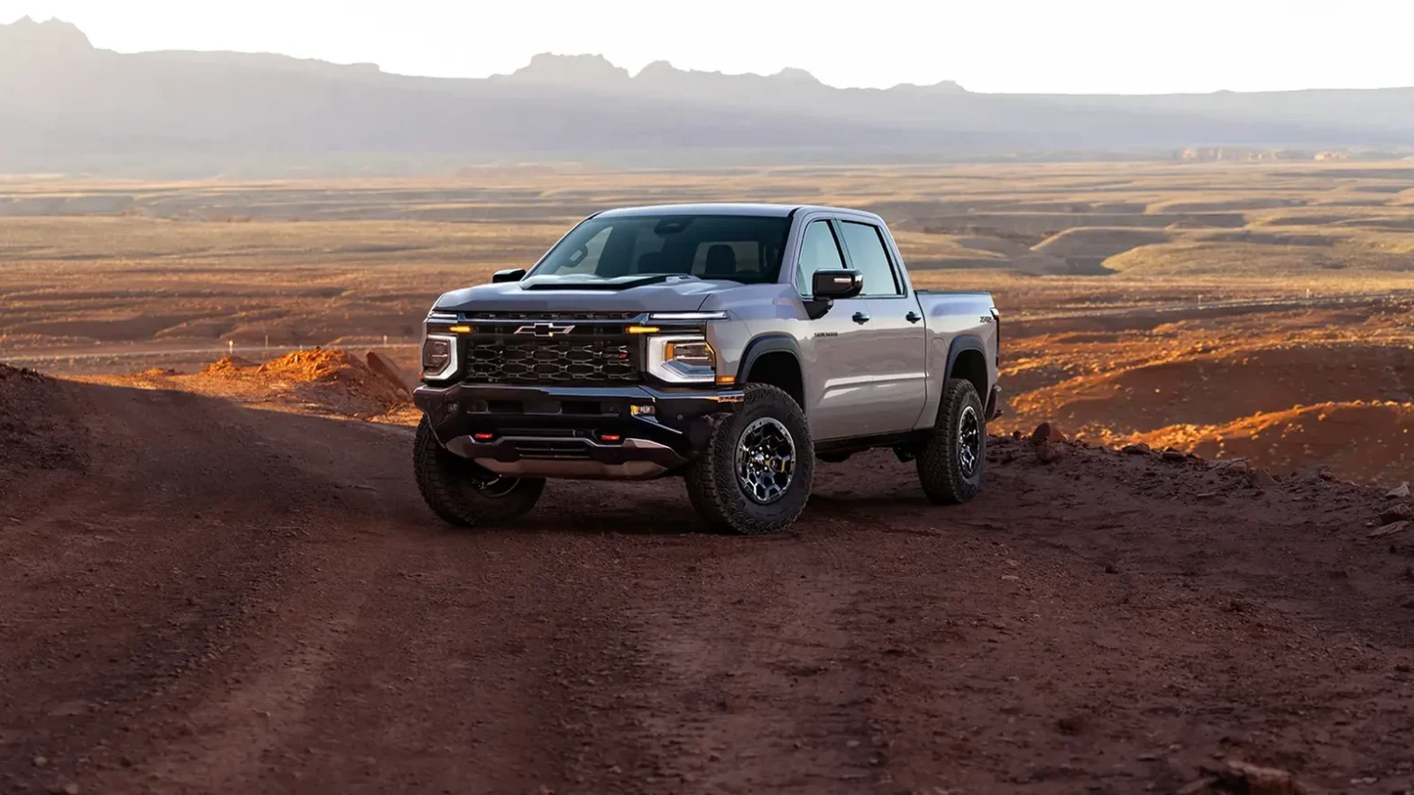What Real Owners Think of the 2027 Silverado and Sierra 1 2027 Chevrolet Silverado 1500 ZR2 pickup truck parked on a dirt road in a desert landscape, viewed from the front three-quarter angle