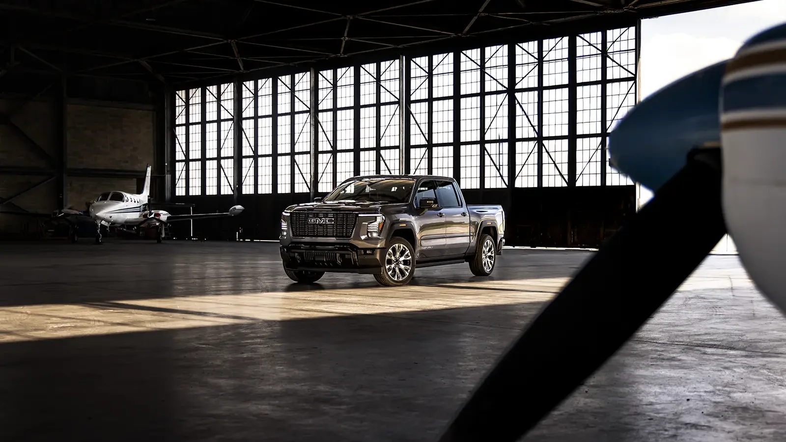 What Real Owners Think of the 2027 Silverado and Sierra 2 2027 GMC Sierra 1500 Denali Ultimate pickup truck parked inside an airplane hangar next to a small propeller aircraft