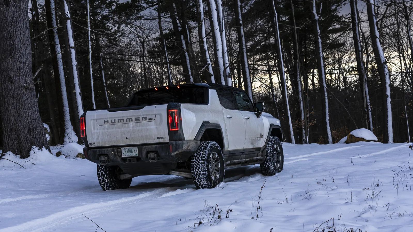 GM Confirms Fix for False Blind Spot Alerts on 19 Models 3 White GMC Hummer EV pickup truck on a snow-covered trail in the woods at dusk, seen from the rear